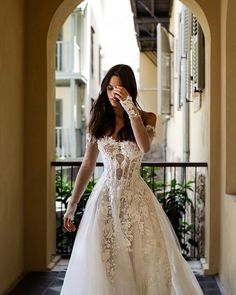 a woman in a white wedding dress is holding her hand up to her face as she walks through an archway