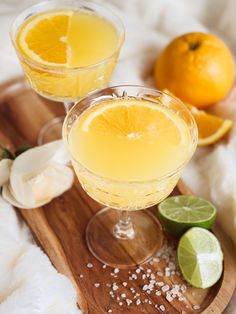 two glasses of lemonade sit on a wooden tray next to an orange and lime