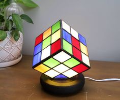 a rubik cube lamp sitting on top of a wooden table next to a potted plant