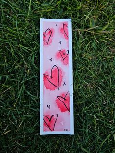 a bookmark with hearts drawn on it laying in the grass