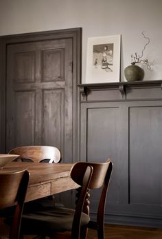 a dining room table and chairs in front of a wooden paneled wall with an old door