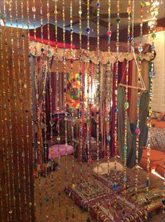 a room filled with lots of beads hanging from the ceiling next to a bed covered in pillows