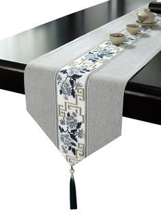 a table runner with blue and white flowers on it, tied to a black dining room table