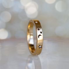 a gold wedding ring with stars and moon designs on the side, against a white background