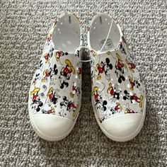 a pair of white shoes with mickey mouses on them are sitting on the carpet