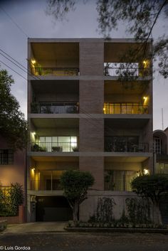 an apartment building lit up at night with lights on the balconies and trees