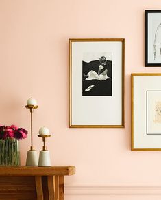 three framed pictures hang on the wall above a table with vases and flowers in front of it