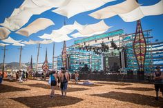 a group of people standing under white umbrellas at an outdoor music festival on a sunny day