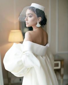 a woman in a white wedding dress with a veil on her head and wearing earrings