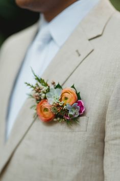 a man wearing a tan suit and orange boutonniere with flowers on the lapel