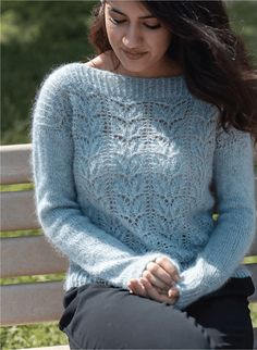 a woman is sitting on a bench wearing a blue knitted sweater and black pants