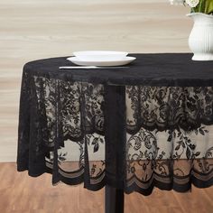 a black table cloth with lace on it and a white vase filled with flowers in the background