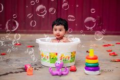 a baby sitting in a tub surrounded by toys and water droplets on the floor,