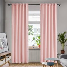 a living room with pink curtains and a grey couch in front of a window that has a potted plant on it