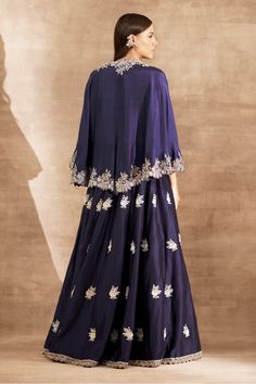 Purple cape style blouse with contrast zardozi embroidery on the neckline and border. Comes with floral embroidered lehenga.
Component: 2
Pattern: Embroidery
Type Of Work: Zardozi
Neckline: V neck
Sleeve Type: Cape Sleeves
Fabric: Silk
Color: Purple
Other Details: 
Zardozi embroidered border and scalloped detail
Cape with cutwork hems
Asymmetrical cape hem
Occasion: Destination Wedding - Aza Fashions Cape Style Blouse, Asymmetrical Cape, Embroidery Zardozi, Purple Cape, Jayanti Reddy, Zardozi Embroidery, Cape Style, Embroidered Lehenga, Embroidered Border