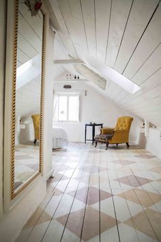 an attic bedroom with white walls and wood flooring is pictured in this image, there are two yellow chairs on the far side of the room