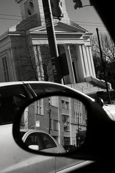 a car's side view mirror is shown in front of a building with a clock tower