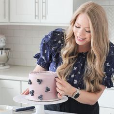 a woman is decorating a pink cake with blue flowers on it while standing in the kitchen