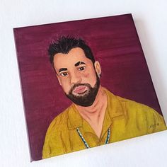 a painting of a man with a beard and yellow shirt on is displayed against a white wall