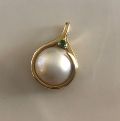 This is a gorgeous Mabé Pearl Pendant surrounded by a 14K gold setting. A beautiful vibrant green Emerald perches on top of the elegant bale. Bale can fit up to a 3mm chain. This is a nice weighty pendant at 4.38 grams. Mabé pearls, also known as blister pearls ,are half-pearls that are cultivated on the inside of a mollusk's shell. A small nucleus, usually made out of mother of pearl, is attached to the shell of the mollusk and left to accumulate nacre over a period that usually runs about two Exquisite Yellow Gold Gemstones For Wedding, Elegant Emerald Pendant Gemstones, Elegant Yellow Gold Diamond Gemstones, Elegant Pear-shaped Gemstones For Anniversary, Elegant Pear-shaped Yellow Gold Gemstones, Elegant Yellow Gold Pear-shaped Gemstones, Elegant Oval Gemstones In 14k Gold, Elegant 14k Gold Gemstones For Formal Occasions, Elegant Round Birthstone Gemstones