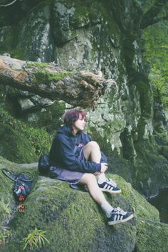 a woman sitting on top of a rock covered in green moss