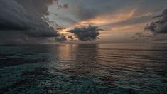 the sun is setting over the ocean with clouds in the sky and water below it