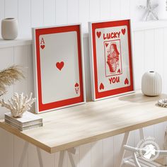 two framed playing cards sitting on top of a wooden table next to a white vase