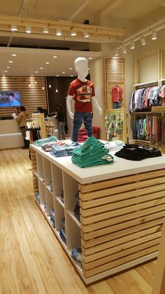 a man standing on top of a counter next to a pile of shirts in a store