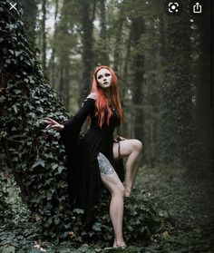 a woman with red hair and makeup is posing in the woods wearing a black dress