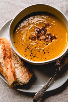 a white plate topped with a bowl of soup next to a piece of bread on top of a table