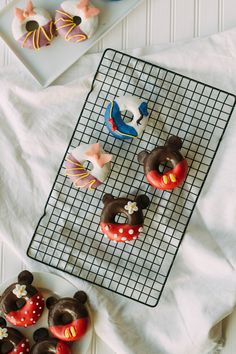 four decorated doughnuts on a cooling rack next to a plate with two pastries