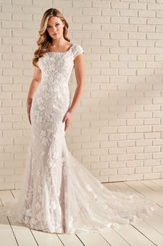 a woman in a white wedding dress standing on a wooden floor next to a brick wall