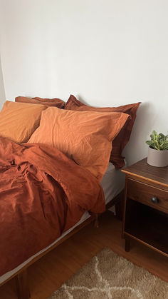 a bed with an orange comforter on top of it next to a night stand