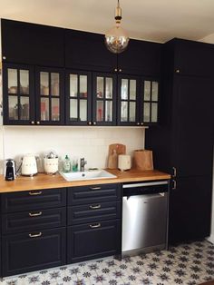 a kitchen with black cabinets and white tile flooring is pictured in this image, there is a dishwasher on the counter next to the sink