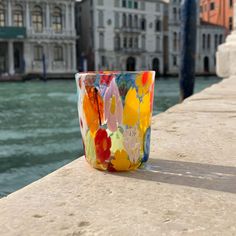 a colorful glass sitting on top of a stone wall next to the water with buildings in the background