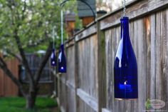 three blue glass bottles hanging from a chain in front of a wooden fence and tree