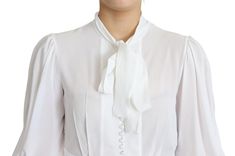 Exude sophistication with this pristine Dolce & Gabbana snow-white blouse, perfect for elevating your wardrobe. Crafted in Italy, this stunning piece showcases an ascot collar and long lantern sleeves. The fitted silhouette is rendered in a sumptuous blend of viscose and elastane, ensuring a comfortable and flattering fit. The front features a polished placket with fabric-covered buttons, adding a touch of elegance. Material: 95% Viscose 5% Elastane Color: White Country of origin: Italy Logo det Designer White Party Blouse, Designer White Blouse For Party, Designer White Blouse For Work, Luxury White Party Tops, Luxury White Office Tops, Designer White Tops For Party, Luxury Long Sleeve Blouse For Wedding, Luxury Long Sleeve Wedding Blouse, Luxury Long Sleeve Tops For Wedding