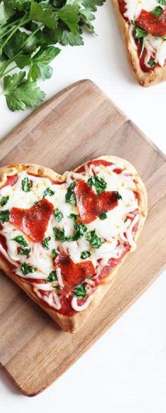 two heart shaped pizzas sitting on top of a cutting board next to parsley