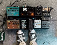 a person's feet with sneakers and pedals next to an array of electronic equipment