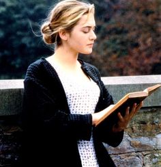 a woman is reading a book on a stone wall