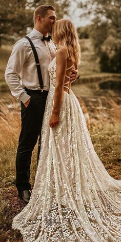 a man and woman standing next to each other in front of some tall grass with trees