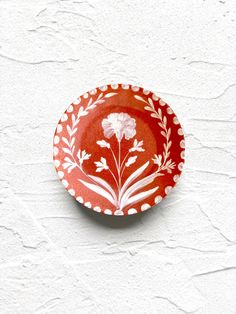 a red and white plate with flowers on it sitting on a table next to a wall