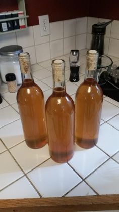 three brown bottles sitting on top of a white tiled kitchen counter next to a blender