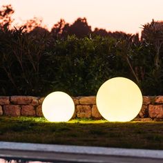 two large white balls sitting next to each other on the grass near a swimming pool