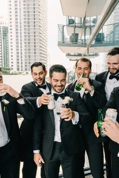 a group of men standing next to each other holding beer cans and wearing tuxedos