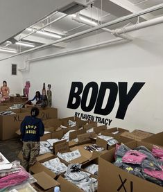 several people are standing around boxes with clothing on them and the words body by raventracy painted on the wall