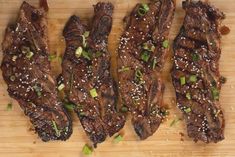 four pieces of steak on a cutting board with green onions and seasoning sprinkles