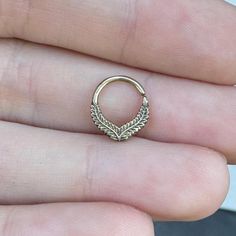 a small gold ring with leaves on it's side is held in someone's hand