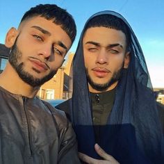 two young men standing next to each other in front of a blue sky and some buildings