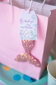 a pink bag with a mermaid tail on it and thank you for christmas tag hanging from the handle